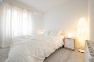 a white bedroom with a large white bed and a table at Apartamento al lado de la Romareda in Zaragoza