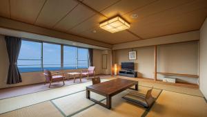 KAMENOI HOTEL Atami Annex في أتامي: غرفة معيشة مع طاولة وكراسي ونافذة كبيرة