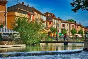 a river with buildings and people walking on a bridge at Appartement à L'Isle-sur-la-Sorgue avec vue sur la ville in LʼIsle-sur-la-Sorgue