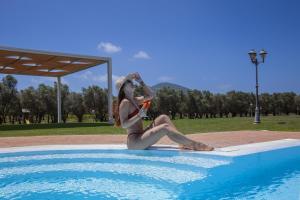 uma mulher de biquíni sentada ao lado de uma piscina em Villa Barbarina Nature Resort em Santa Maria la Palma