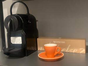 pomarańczowy kubek kawy siedzący na stole obok pudełka w obiekcie Rivacentro 2 w mieście Riva del Garda