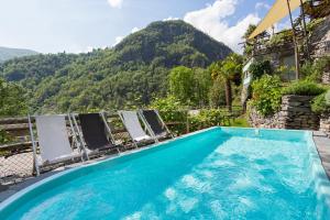una piscina con sillas y montañas en el fondo en Rustici della Verzasca Ferien Wohnungen en Vogorno