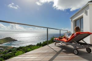 a woman sitting in a chair on a balcony with a laptop at Villa La Vue - Vue panoramique sur les lagons in Gustavia