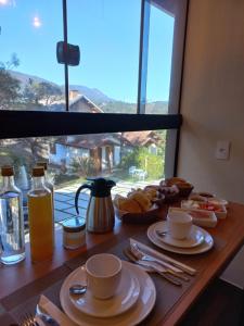 uma mesa com copos e pratos de comida e uma janela em Terrace Chalés em Monte Verde