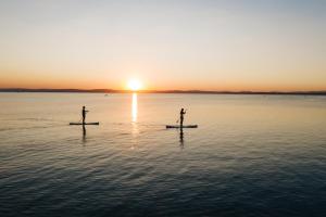 Zwei Leute sind Paddleboarding auf dem Wasser bei Sonnenuntergang. in der Unterkunft Tópart Hotel in Balatonvilágos