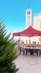 een tafel en stoelen onder een rode tent met een klokkentoren bij Qandeel - Dar Botto in Bethlehem