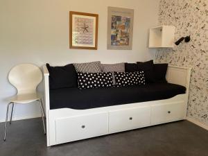 Cama blanca con almohadas negras y silla blanca en Liten ”stuga” en Falkenberg