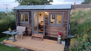 eine Hütte mit einer Holzterrasse mit einem Stuhl und einem Tisch in der Unterkunft Rhodes To Serenity - Mermaid Shepherds Hut in Stoke on Trent