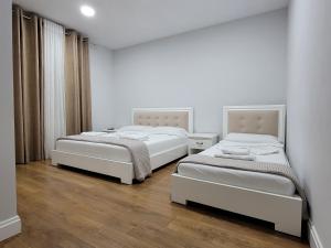 Habitación con 2 camas, paredes blancas y suelo de madera. en Hotel Taverna Zisi, en Ersekë