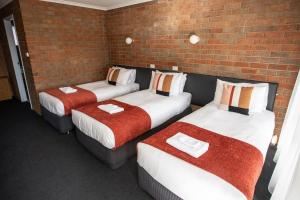 three beds in a room with a brick wall at Moama Motel in Moama