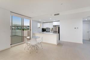 a white kitchen with a glass table and chairs at KULA Sydney Airport in Sydney