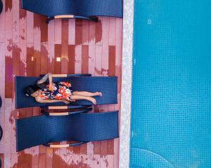 Ari Grand Hotel & Spa في دانجيثي: امرأة مستلقية على كرسي بجوار حمام السباحة