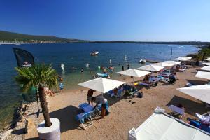 a beach with umbrellas and people in the water at Apartments with a parking space Kornic, Krk - 415 in Kornić
