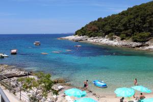 grupa ludzi na plaży z niebieskimi parasolami w obiekcie Apartments and rooms with parking space Mali Losinj (Losinj) - 2497 w miejscowości Mali Lošinj