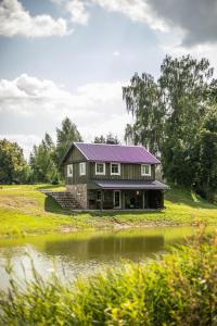 uma casa com um telhado roxo ao lado de um lago em Arčiau Gamtos Virinta em Kurkliai