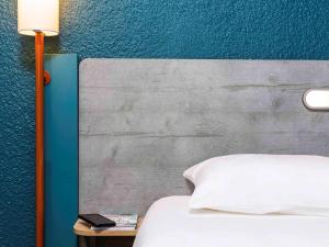 a bed with a white pillow next to a blue wall at ibis budget Paris Porte d'Italie Est in Le Kremlin-Bicêtre