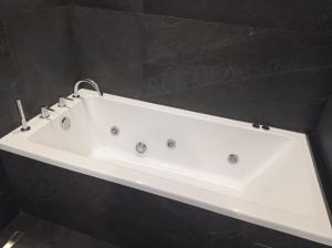 a white bath tub in a bathroom with black tiles at Petra Hotel in Agia Galini