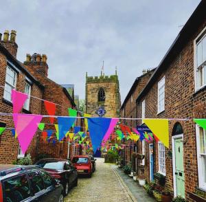 a street with colorful flags and cars parked in front of buildings at Feather and Twigs Cottage, Croston in Croston
