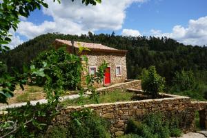 uma pequena casa de pedra com uma porta vermelha em Beija Rio Charming House em Ferreira do Zêzere