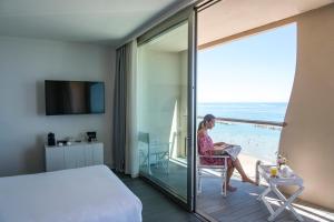 une femme assise dans une pièce avec vue sur l'océan dans l'établissement Hotel Excelsior, à Pesaro