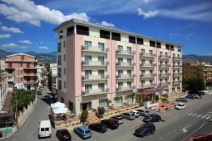 a pink building with cars parked in a parking lot at Hotel Corallo in Villapiana