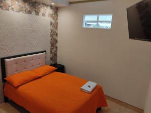 a bedroom with a bed with an orange blanket and a television at Aparta-Hotel El Dorado in Aguadas