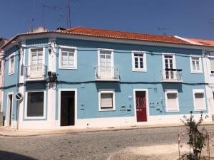 een blauw gebouw met witte ramen en een rode deur bij Casa do Mercado in Alcácer do Sal