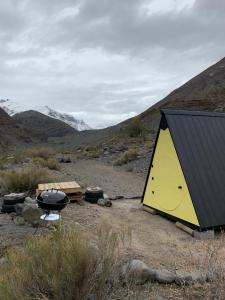 une tente jaune et noire dans un champ avec des montagnes dans l'établissement Glamping Roots del Yeso, à Los Chacayes