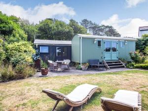 a green tiny house with chairs and a patio at The Shepherd's Hut in Aberdyfi