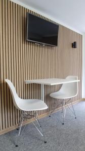 dwa białe krzesła i stół i telewizor na ścianie w obiekcie Noclegi Malta Poznań w Poznaniu