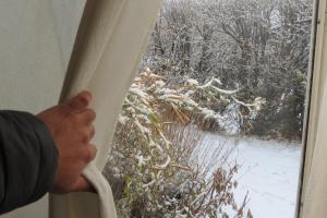 een persoon die uit een raam kijkt naar een sneeuwbedekte tuin bij AONIKENK HOSTEL in El Calafate