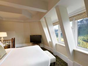 a bedroom with a bed and a tv and two windows at Fairmont Banff Springs in Banff