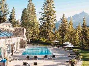 uma piscina de resort com cadeiras, guarda-sóis e árvores em Fairmont Banff Springs em Banff