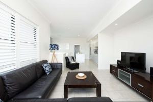 a living room with a black leather couch and a tv at Beachfront Eight in Mollymook