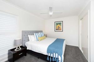 a white bedroom with a bed and a ceiling fan at Beachfront Eight in Mollymook