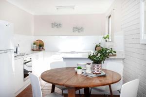 cocina blanca con mesa de madera y sillas blancas en Surfmist One on Mollymook, en Mollymook