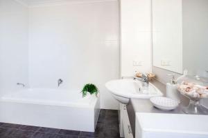 a white bathroom with a sink and a bath tub at Beachfront Four in Mollymook