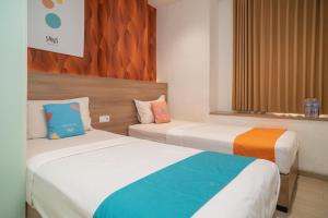 two beds in a hotel room with colorful pillows at Sans Hotel Kupang Indah Surabaya by RedDoorz in Kupang