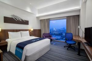 ジャカルタにあるホリデイ イン エクスプレス ジャカルタ プルイト シティゲートのベッド、デスク、窓が備わるホテルルームです。