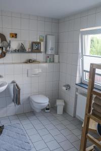 La salle de bains est pourvue de carrelage blanc, de toilettes et d'un lavabo. dans l'établissement Deine-Eifel-Ferienwohnung, à Feusdorf