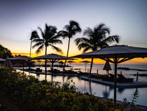 - une piscine bordée de parasols et de palmiers sur une plage dans l'établissement Fisherman's Cove Resort, à Bel Ombre