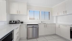 a white kitchen with white cabinets and a window at Surfspray 4 Pebbly Beach in Forster