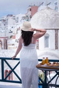 una donna con un vestito bianco e un cappello sul balcone di DELION VIEW HOTEL a Firà