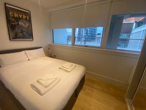 a bedroom with a bed with white sheets and windows at 90s RETRO 1Bed Studio Apartment Wembley Park London Private GYM & CINEMA & Netflix Perfect for Solo & Coupled Travellers in London