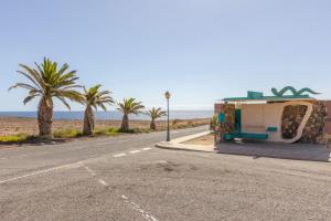 een lege weg naast een strand met palmbomen bij IRIS Holiday House Fuerteventura in Costa de Antigua