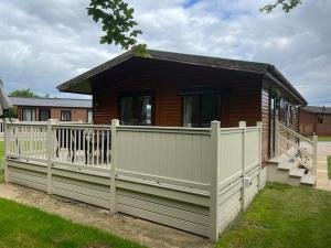 a wooden house with a white fence and a porch at Woodland Lodge With Hot Tub in Malton