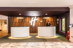 Un uomo in piedi davanti a un bancone in una hall di Holiday Inn Guildford, an IHG Hotel a Guildford