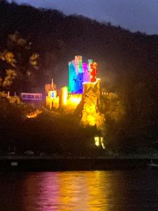 a castle is lit up at night on the water at Das Loreley Weinstuebchen in Sankt Goarshausen