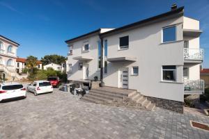 a white house with cars parked in a parking lot at Apartment Odore di Mare with beautiful garden in Krk