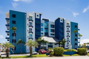 een blauw appartementencomplex met palmbomen op een parkeerplaats bij Coconut Palms Beach Resort II a Ramada by Wyndham in New Smyrna Beach